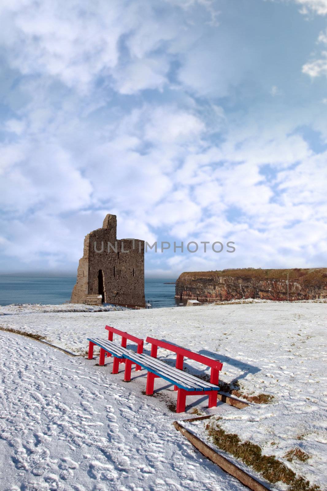 a seasonal snow covered view of atlantic ocean and ballybunion castle with red benches on a frosty snow covered winters day