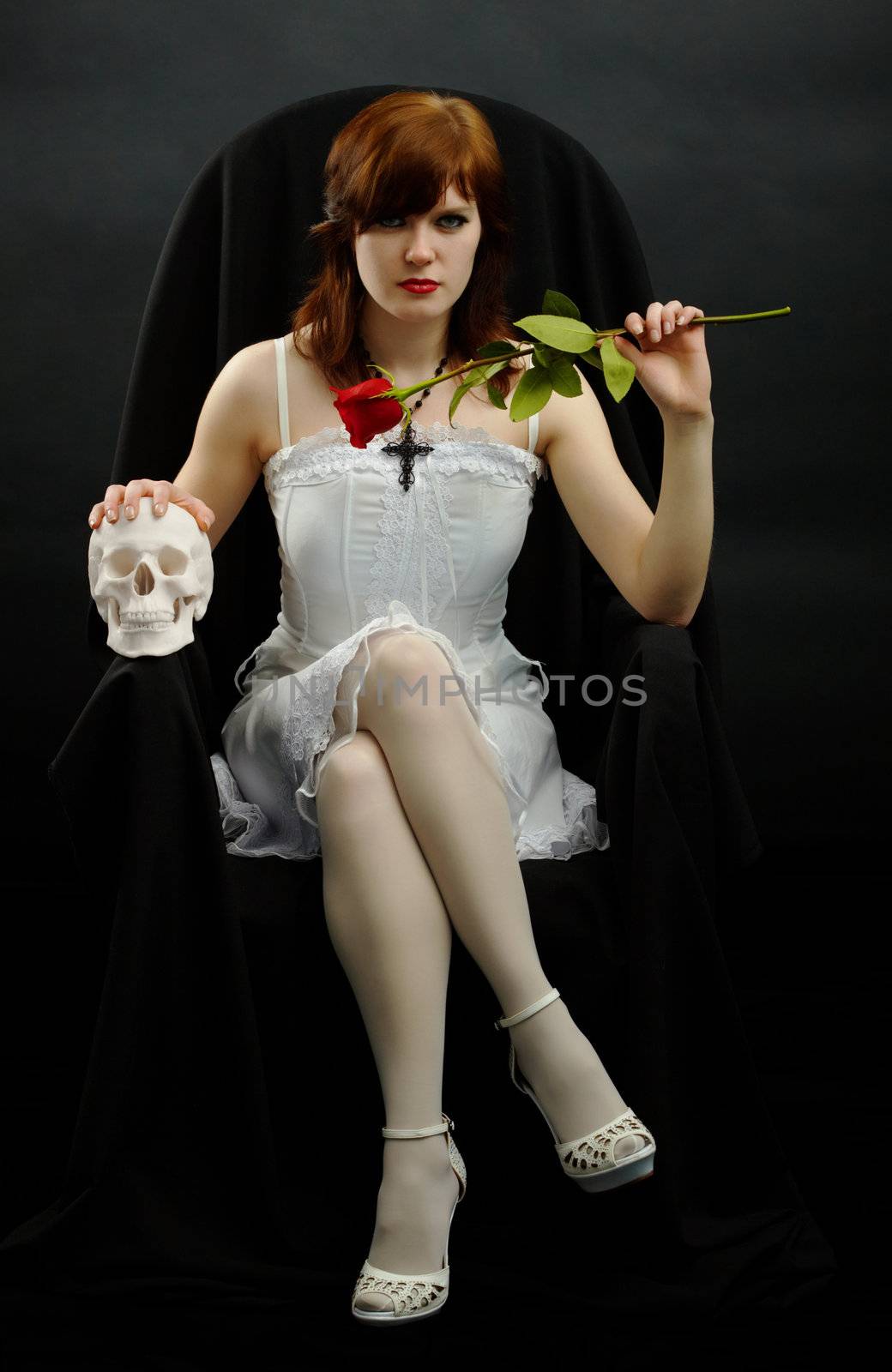 A young girl sits in a black chair with a rose and skull