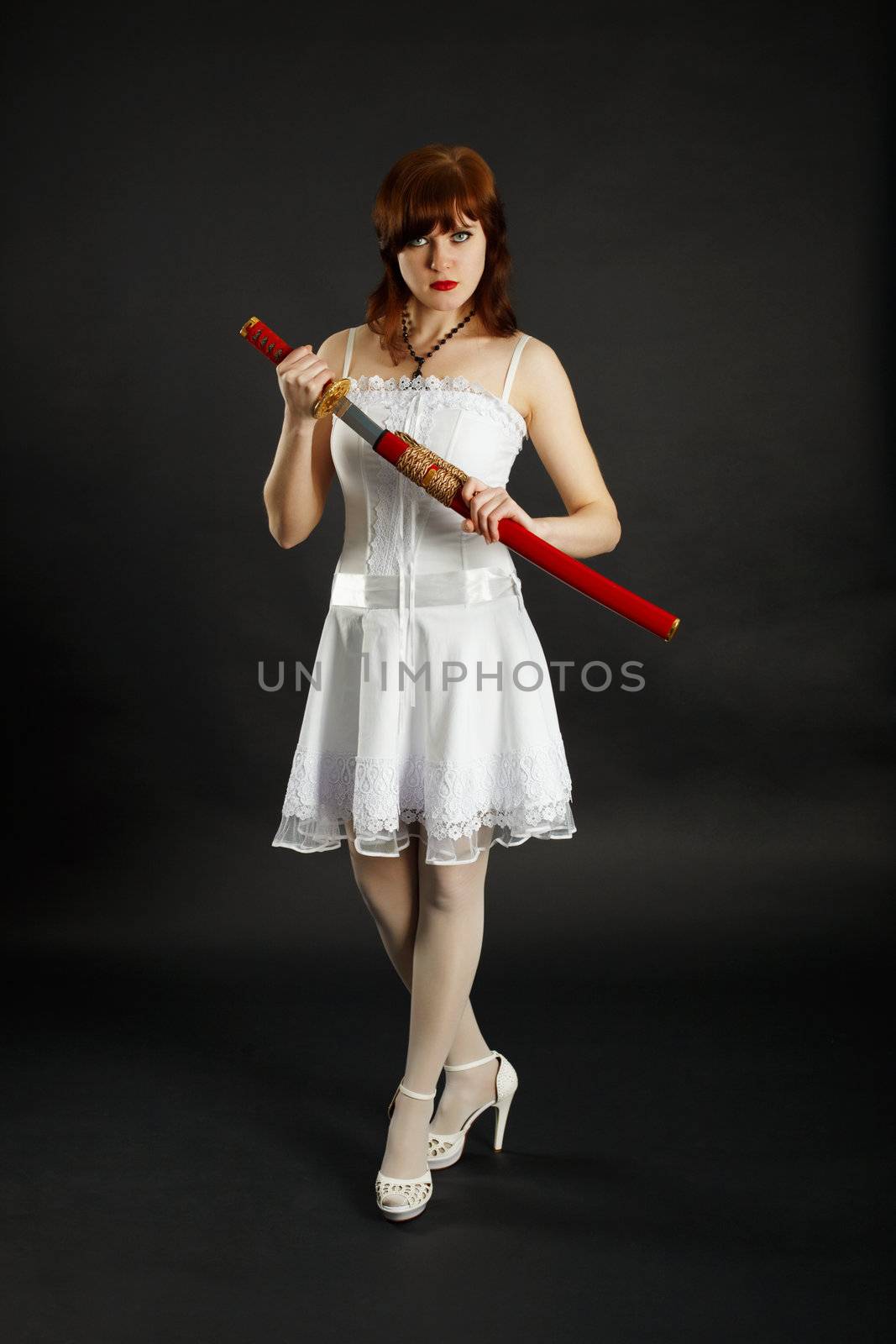 A young girl stands on a black background with a sword