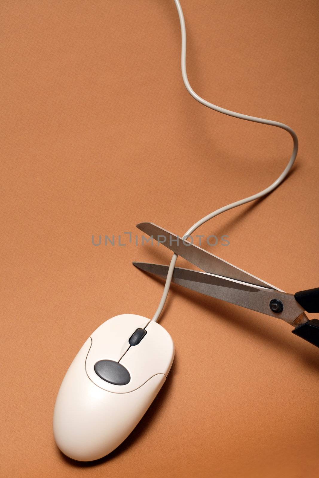 Scissors cutting cable of computer mouse on brown background