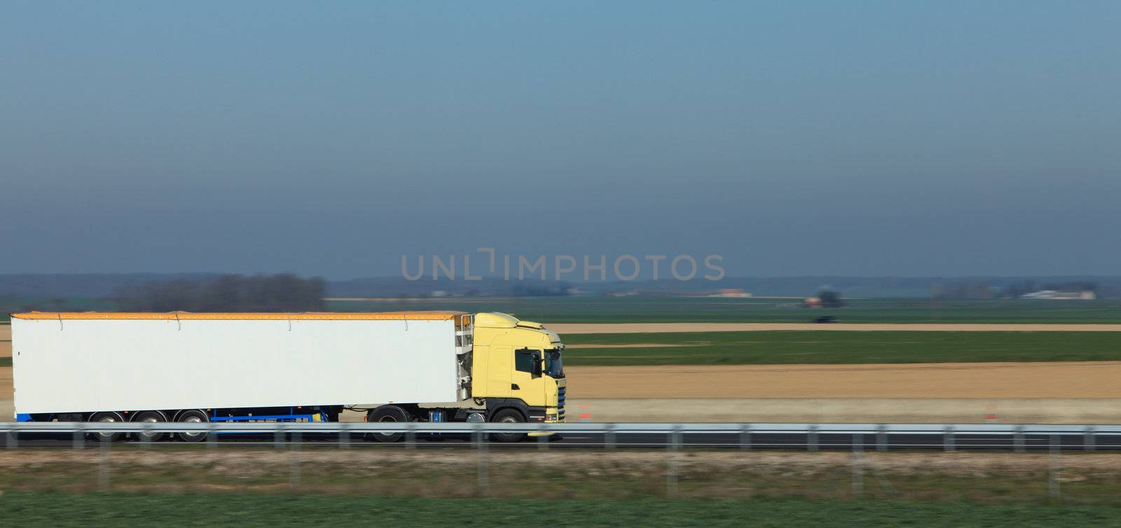 Panning image of a big white track on a highway in a plain area.