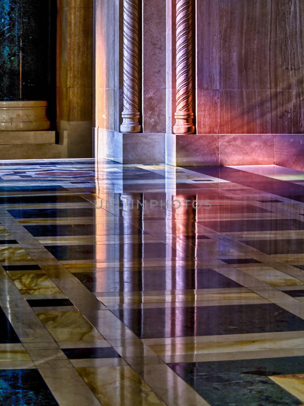 Colorful light from a stained glass window in a cathedral falls on the polished marble of the church illuminating the carved pillars and reflecting in floor