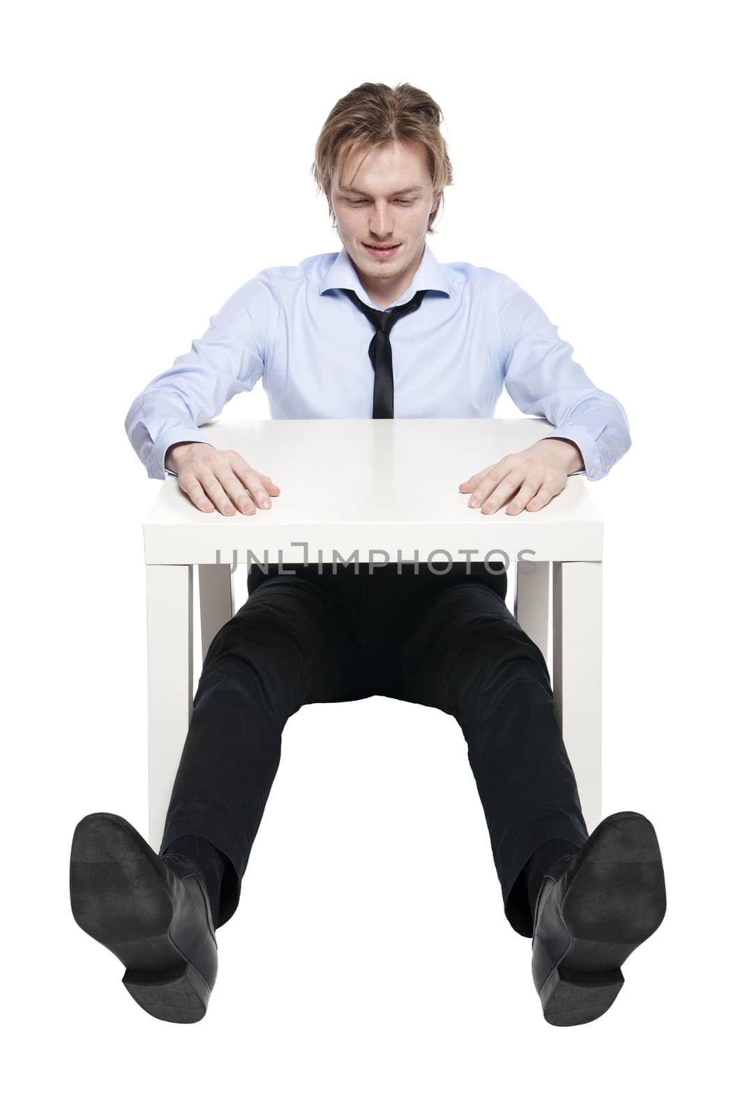 Young businessman, office worker or student sitting at funny small table. Studio photo, isolated.