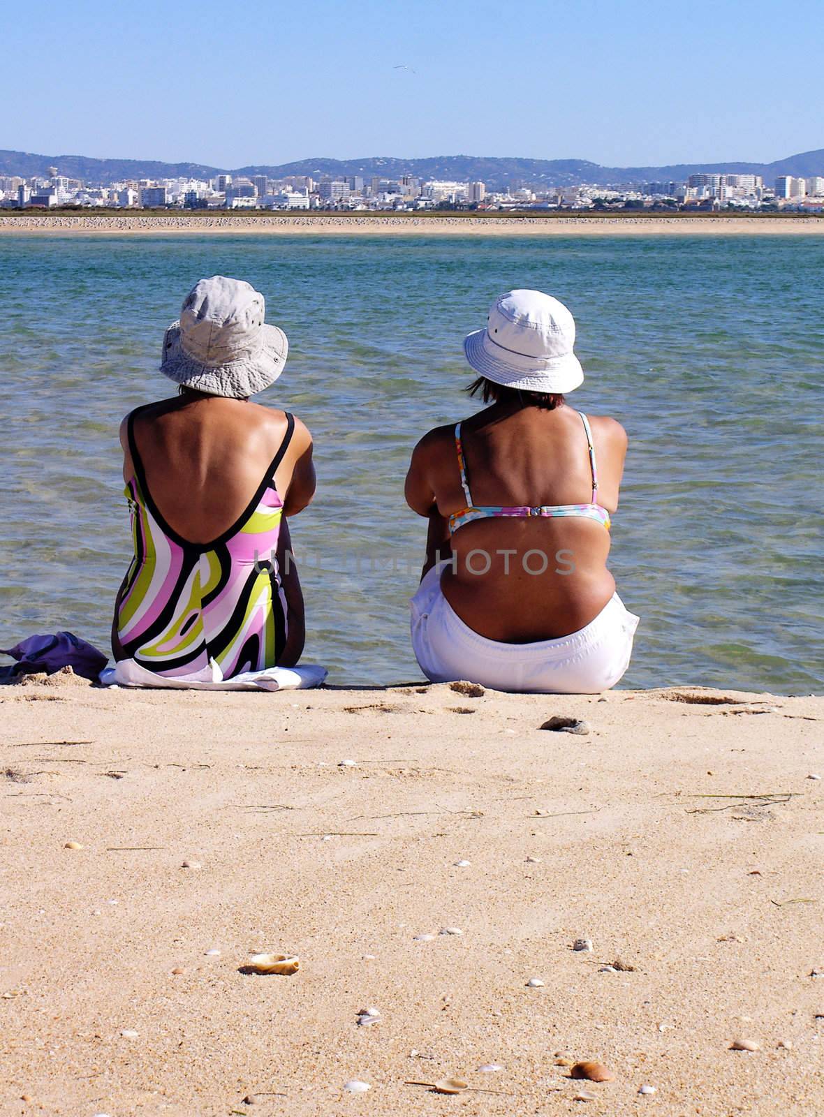 Two middle age ladies relaxing at the beach watching the sea and city...