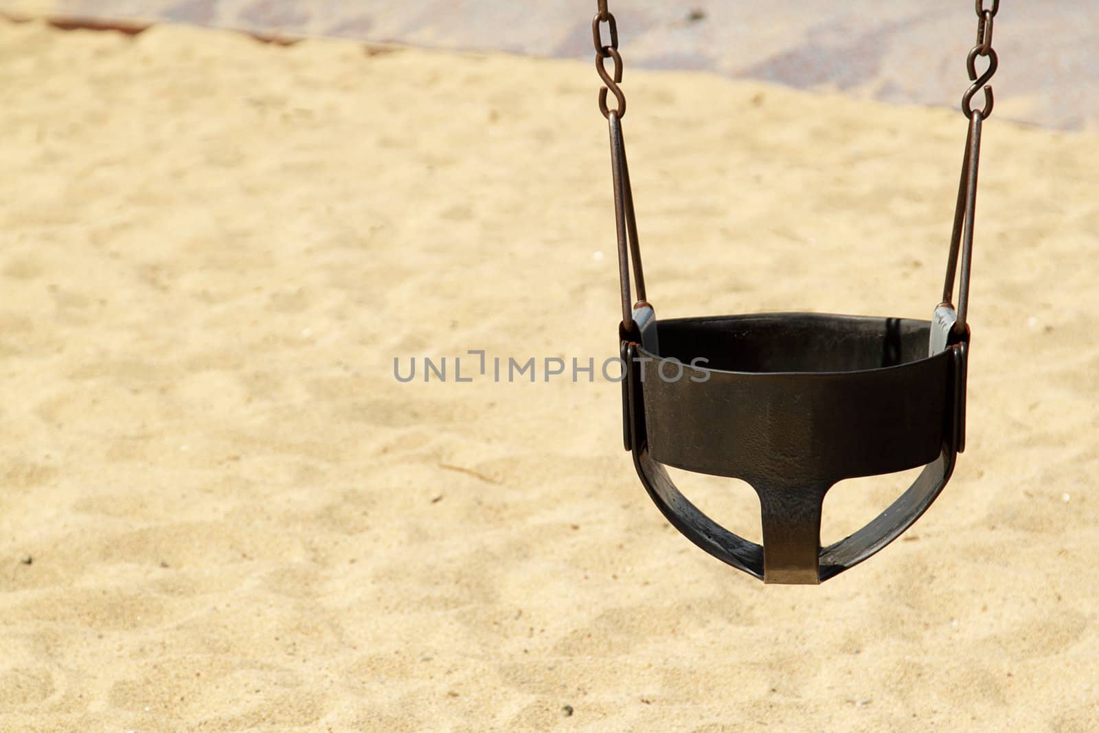 Black swing on the childrens playground with sand as a background on sunny day