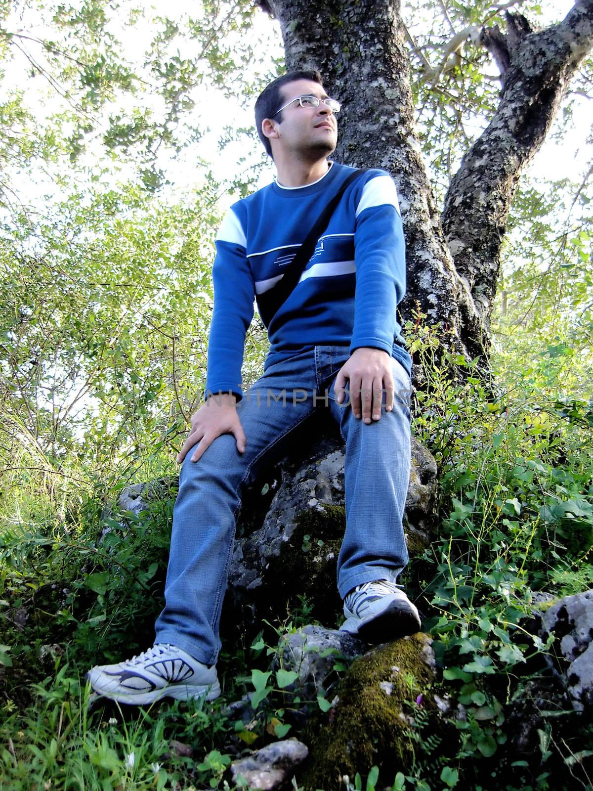 Young man sitting on a rock in front of a tree apreciating the nature.