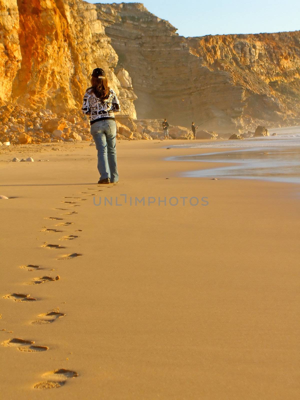 young woman walking on the Tonel Beach near Sagres, Portugal, leaving a footstep trail on the sand.