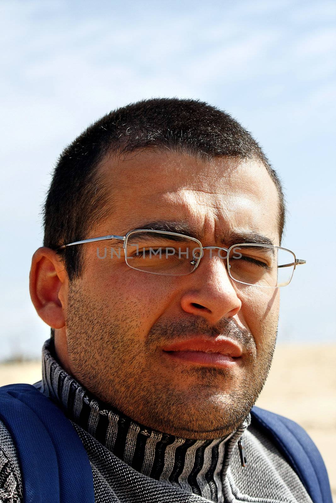 View of a young man with eyes closed because of the sun with backpack.