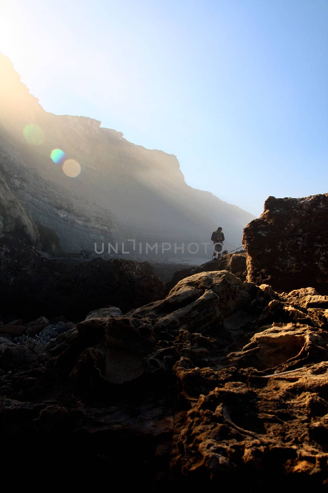 Fisherman on the lower right side being bathed with morning ray lights through the mystical fog over the rocky shore.