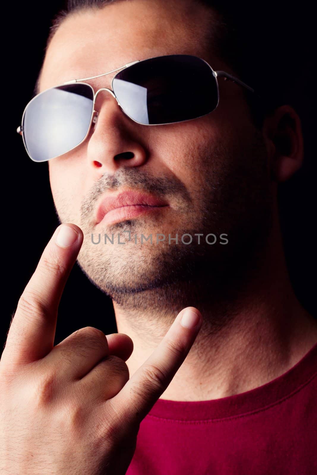 Close detail view of a young male man with dark shades making a sign with the hand isolated on a black background.