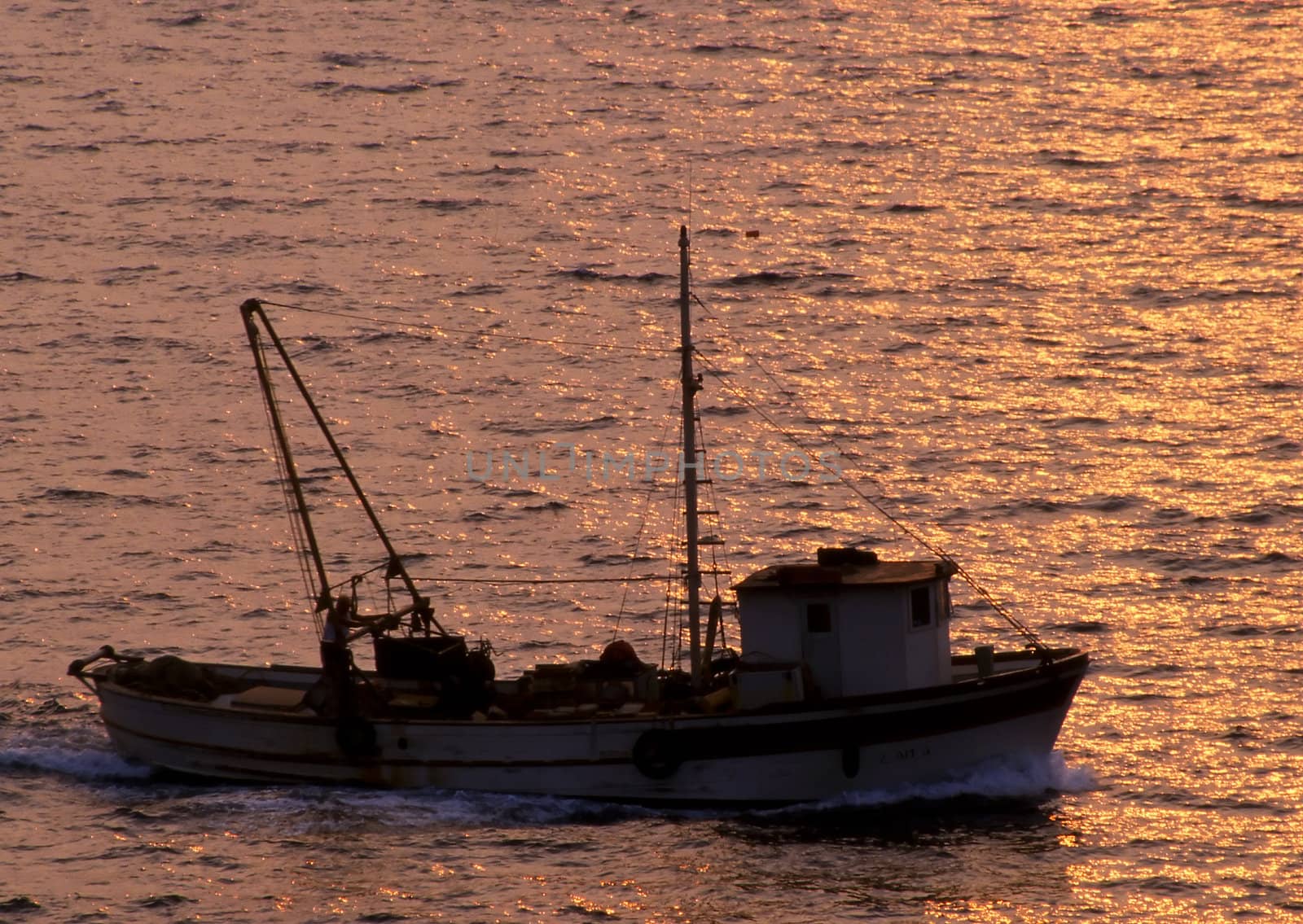 A greek fishing boat makes its way home with the sun shining in the sea by runamock