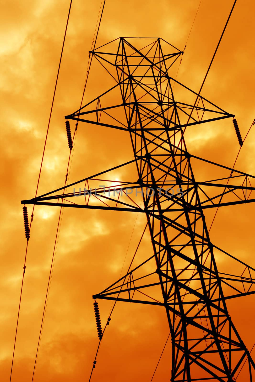 The silhouette of a power line tower against an ominous orange sky.