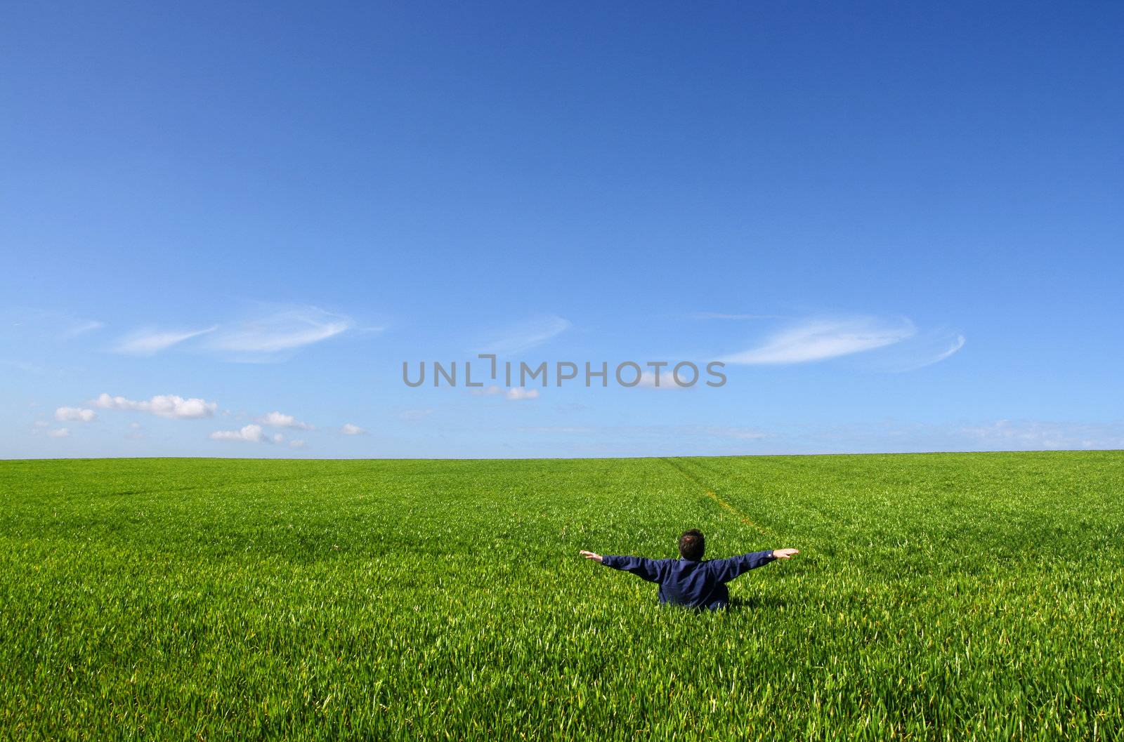 A man sitting alone in a green field, with open arms