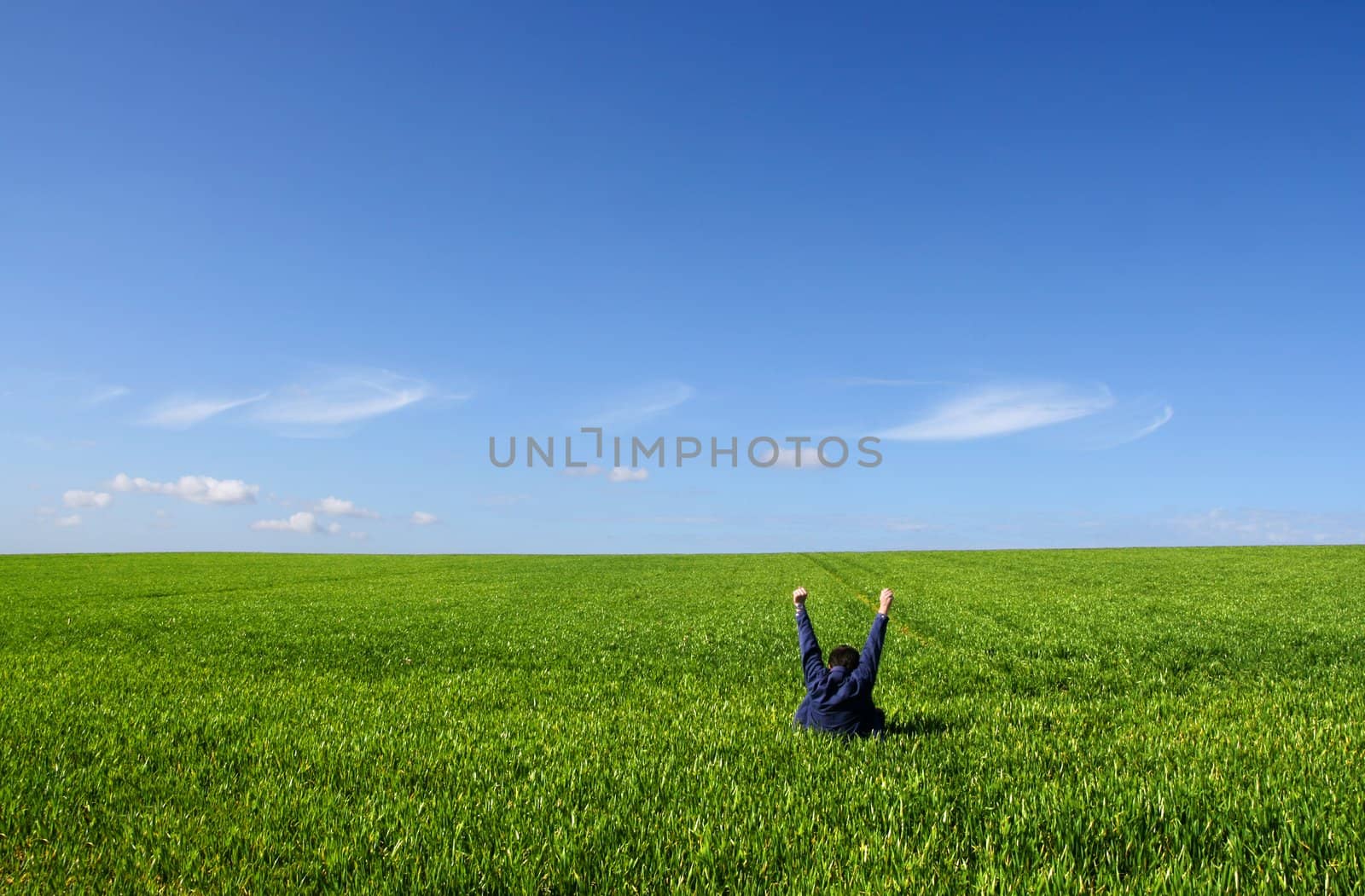 A man sitting alone in a green field, with lifted V arms
