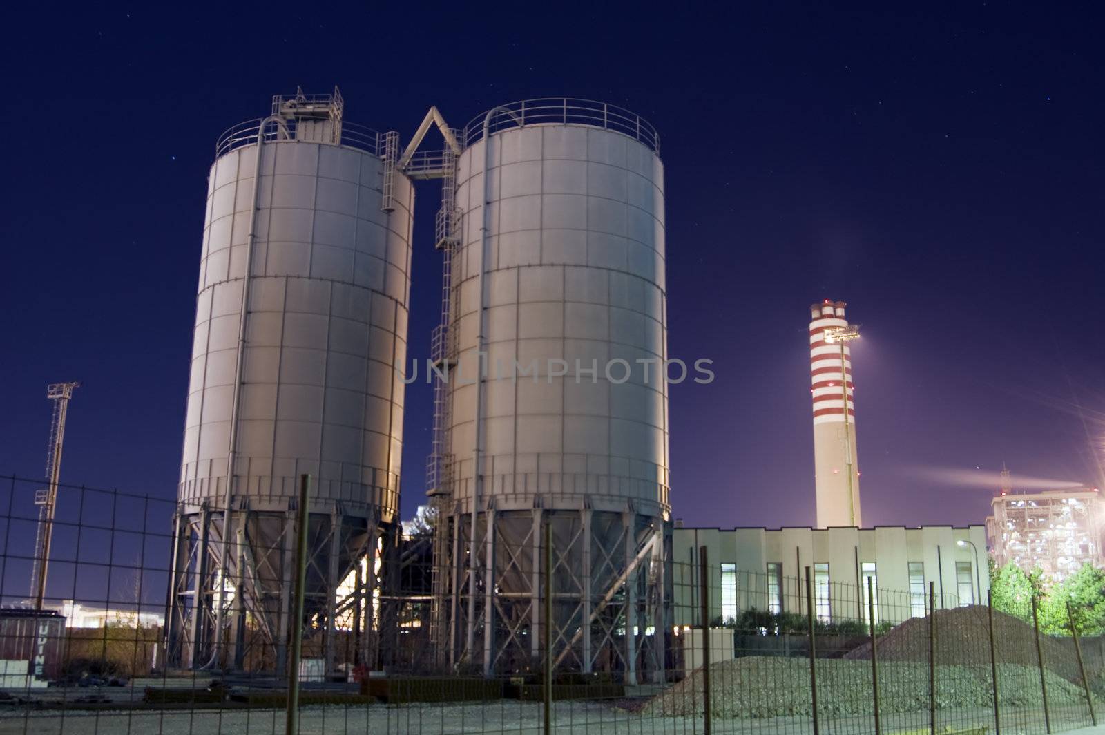 Construction site with silos and chimney by night