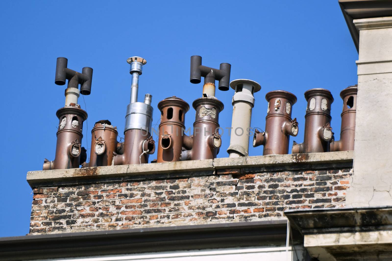 Line of old chimneys on a building rooftop agaist a blue sky