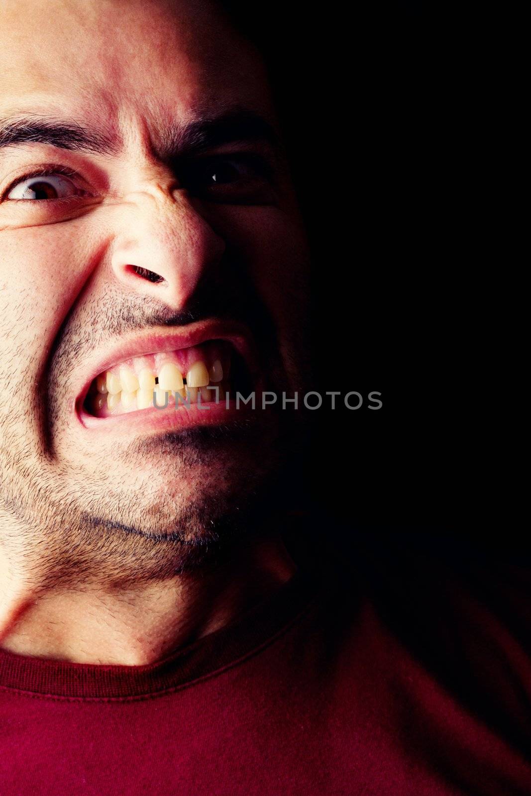 Close detail view of a furious young male man isolated on a black background.