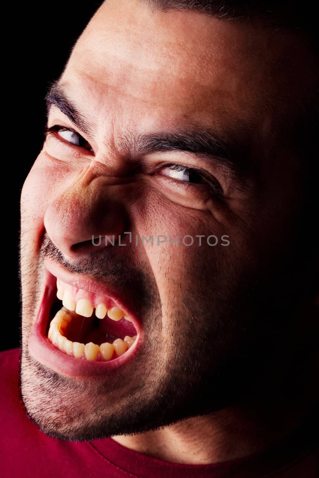 Close detail view of a angry young male man isolated on a black background.