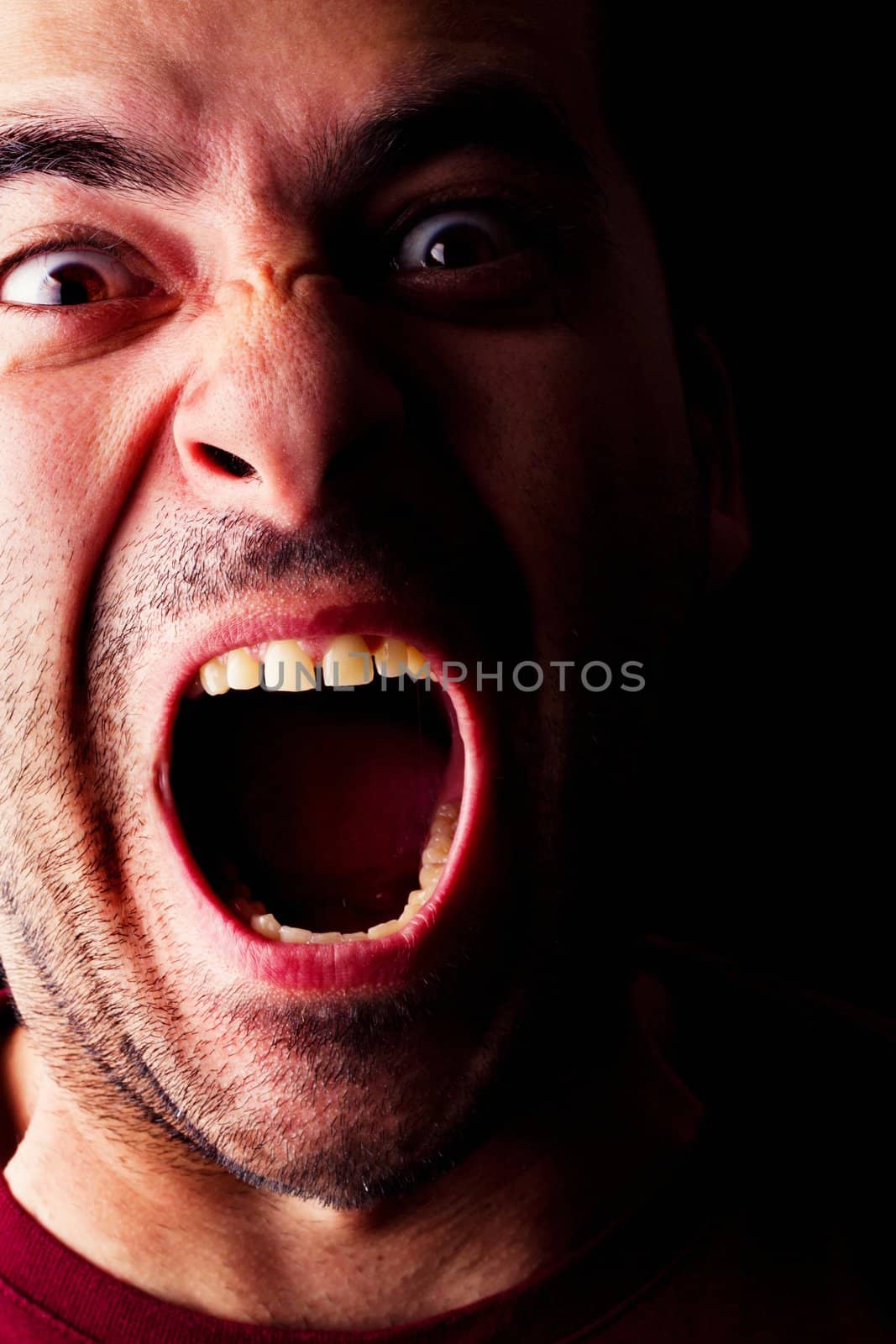 Close detail view of a mad young male man isolated on a black background.