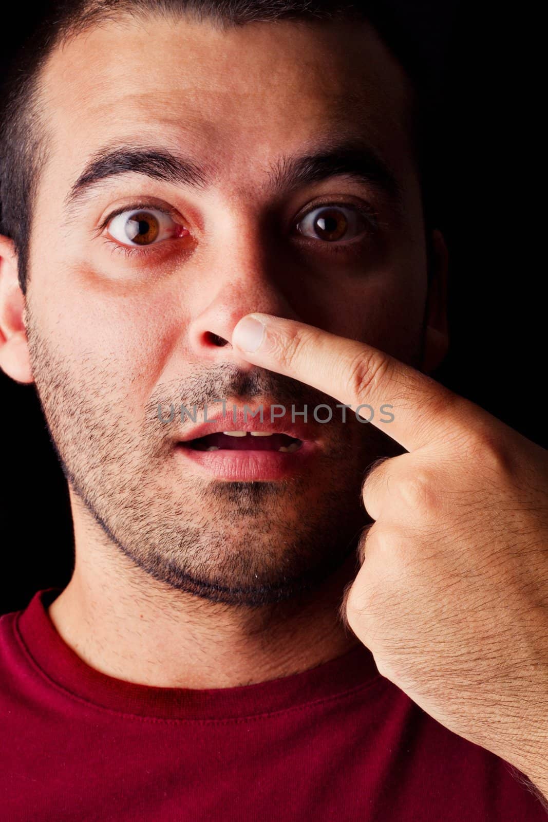 Close detail view of a funny young male man with finger on nose isolated on a black background.