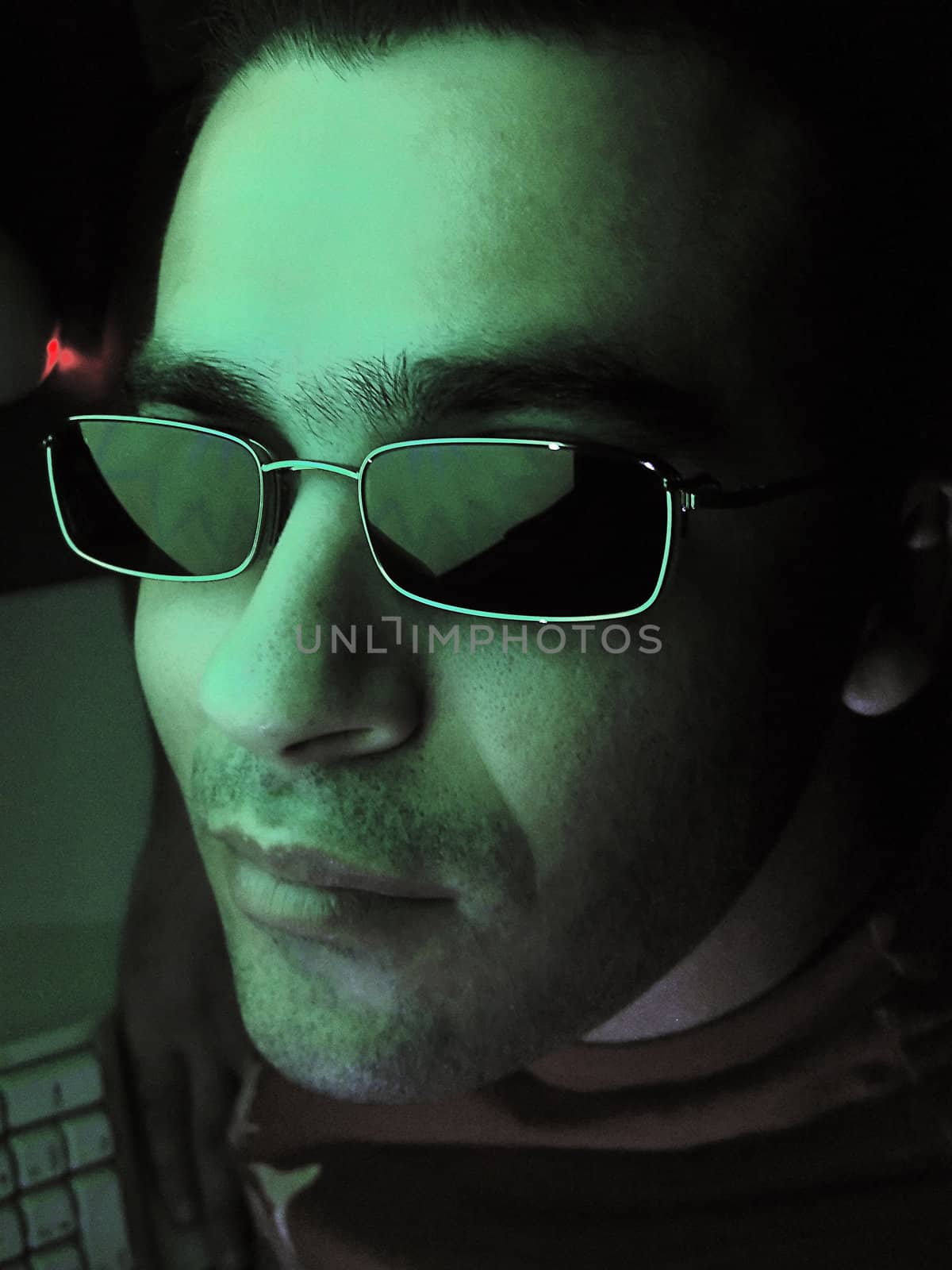 young man looking at camera next to computer on a nocturnal setting.