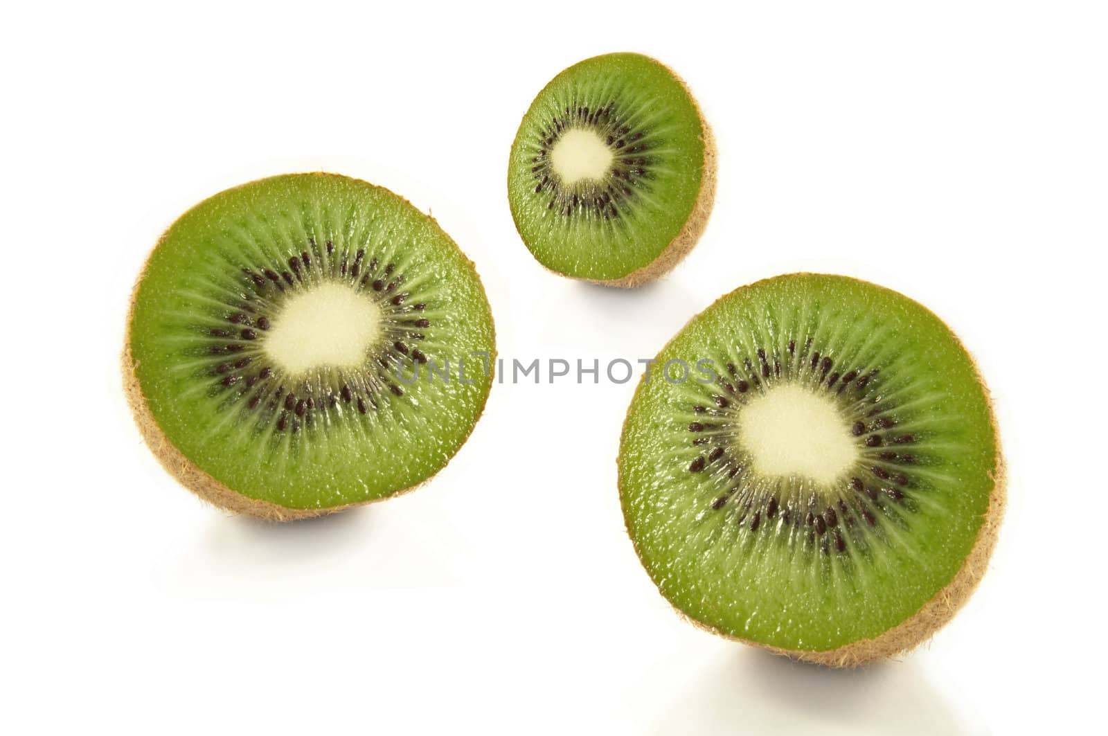Low and close capturing three fresh kiwi fruit halves arranged over white.