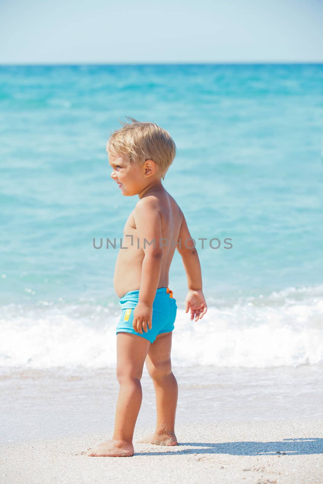 Cute little boy stands in front of the blue sea