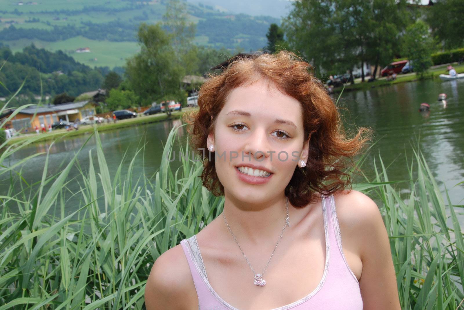 Beautiful red haired woman smiling at little lake in summer.