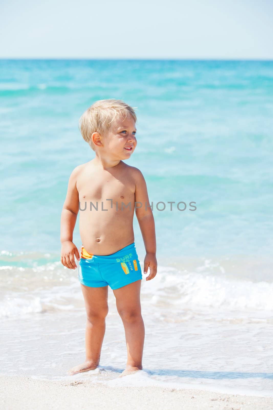 Cute little boy stands in front of the blue sea