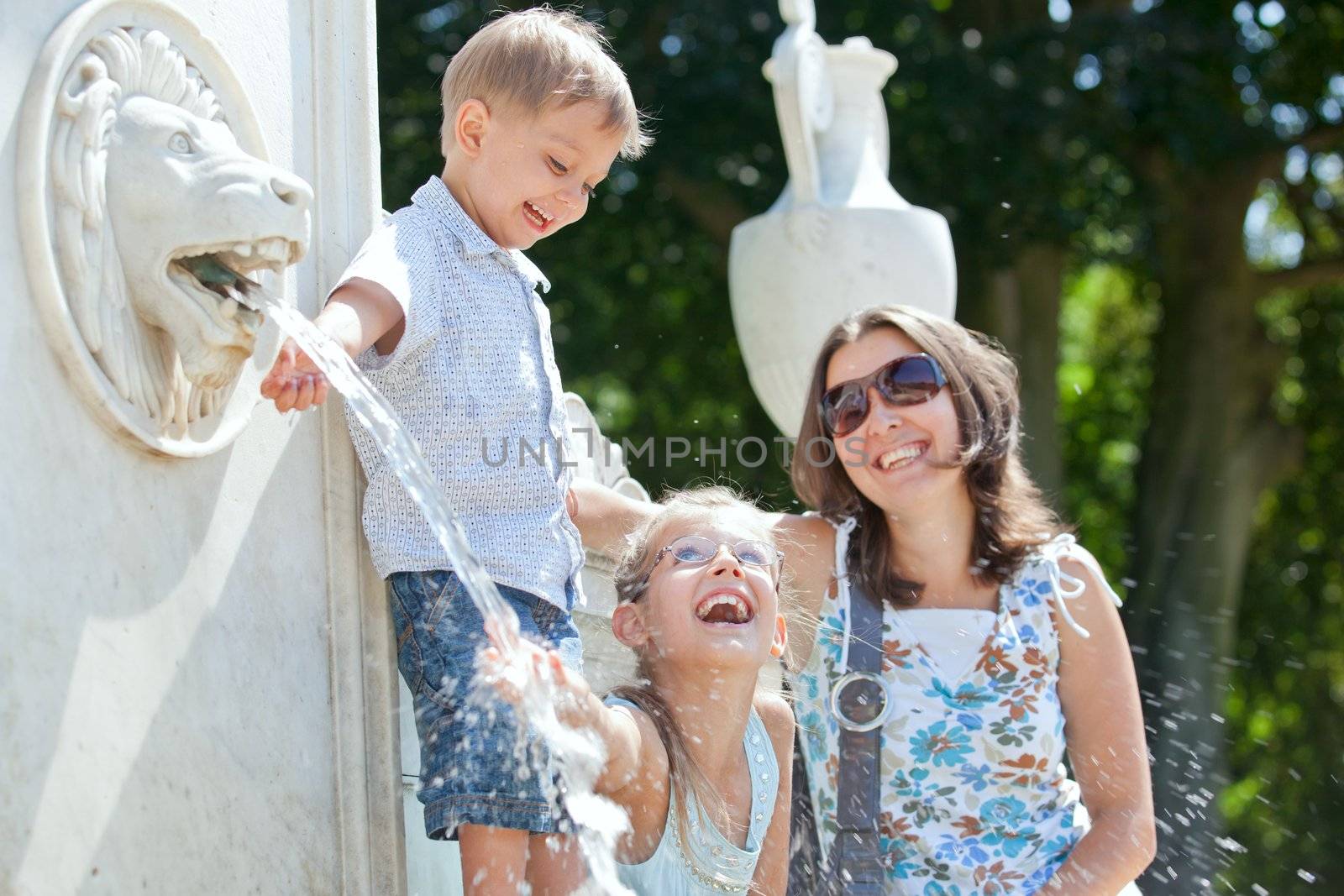 Beautiful Mother with her kids playing with water in fountain