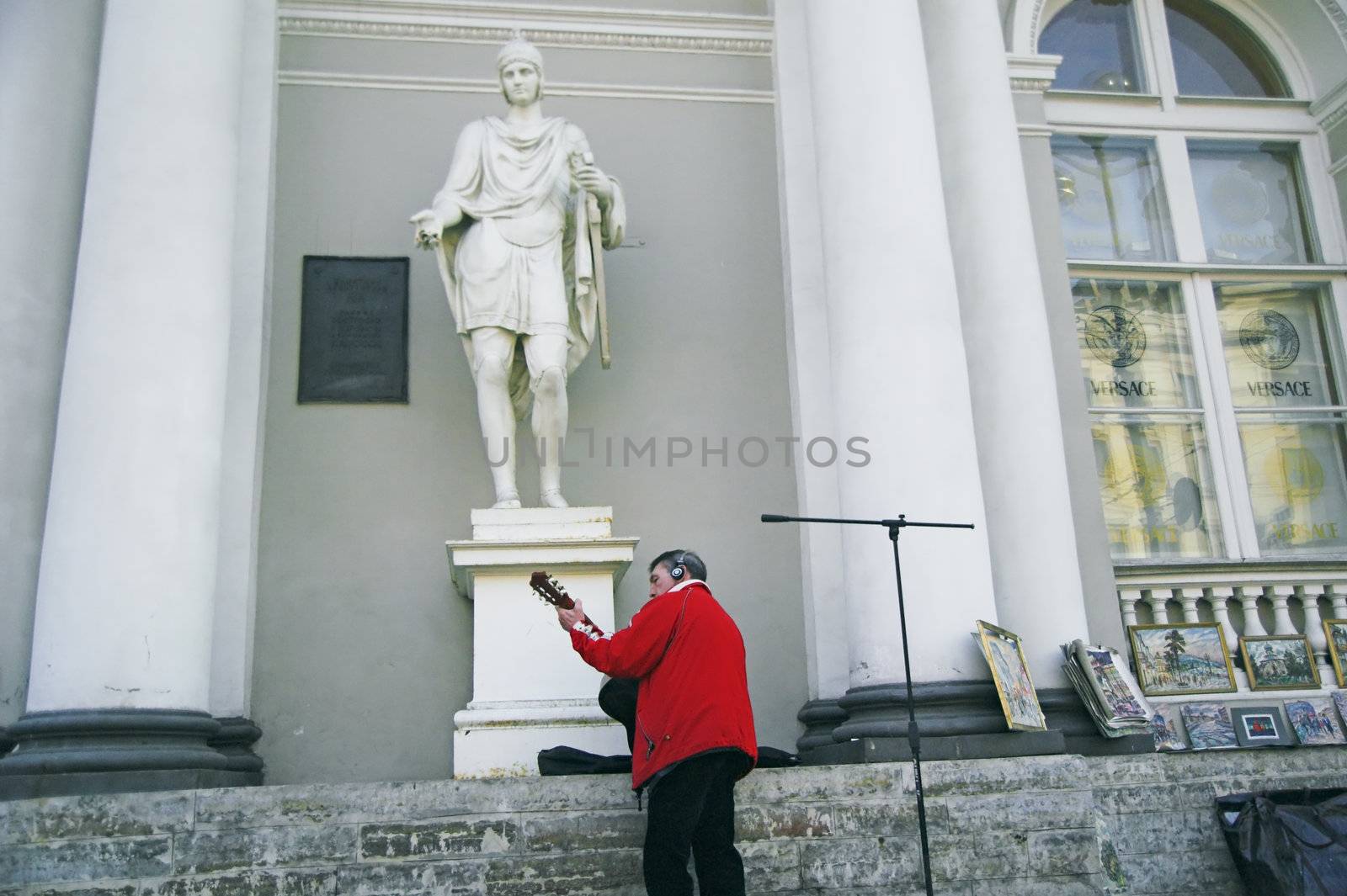 ST PETERSBURG, RUSSIA-MARCH 31, 2008: Street musician playing guitar by sidewalk in front of antique building in Saint Petersburg, Russia