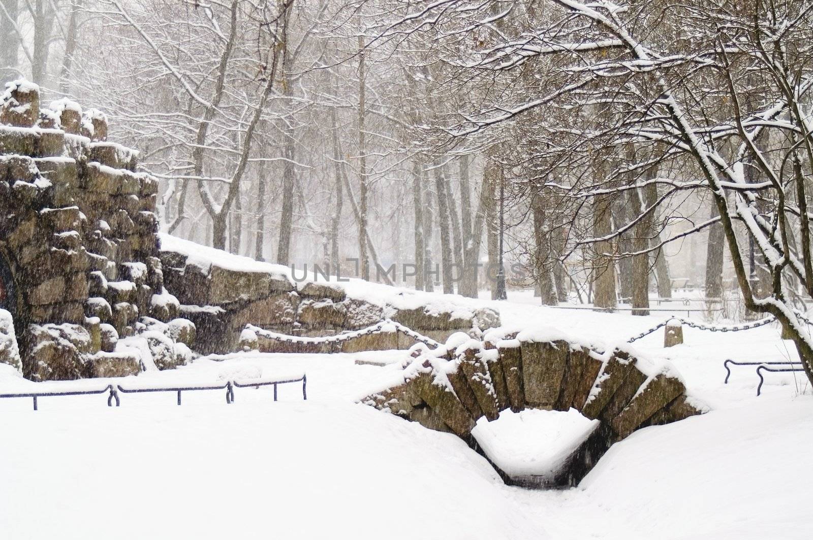 A grotto and a small bridge in a winter park at snowfall.