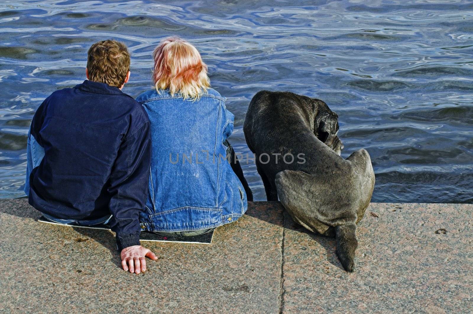 A couple and a dog sitting at the embankment of Neva river in Saint Petersburg, Russia.