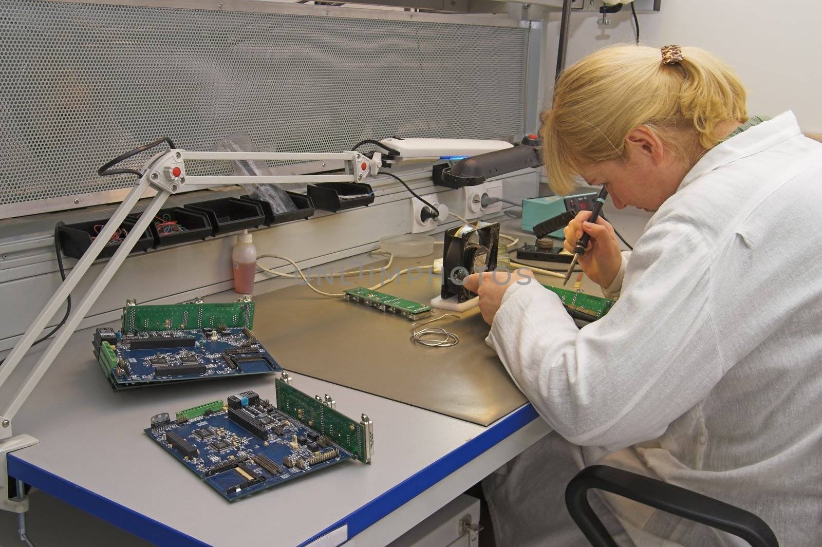 Engineer working with circuits - A woman engineer solders circuits sitting at a table.