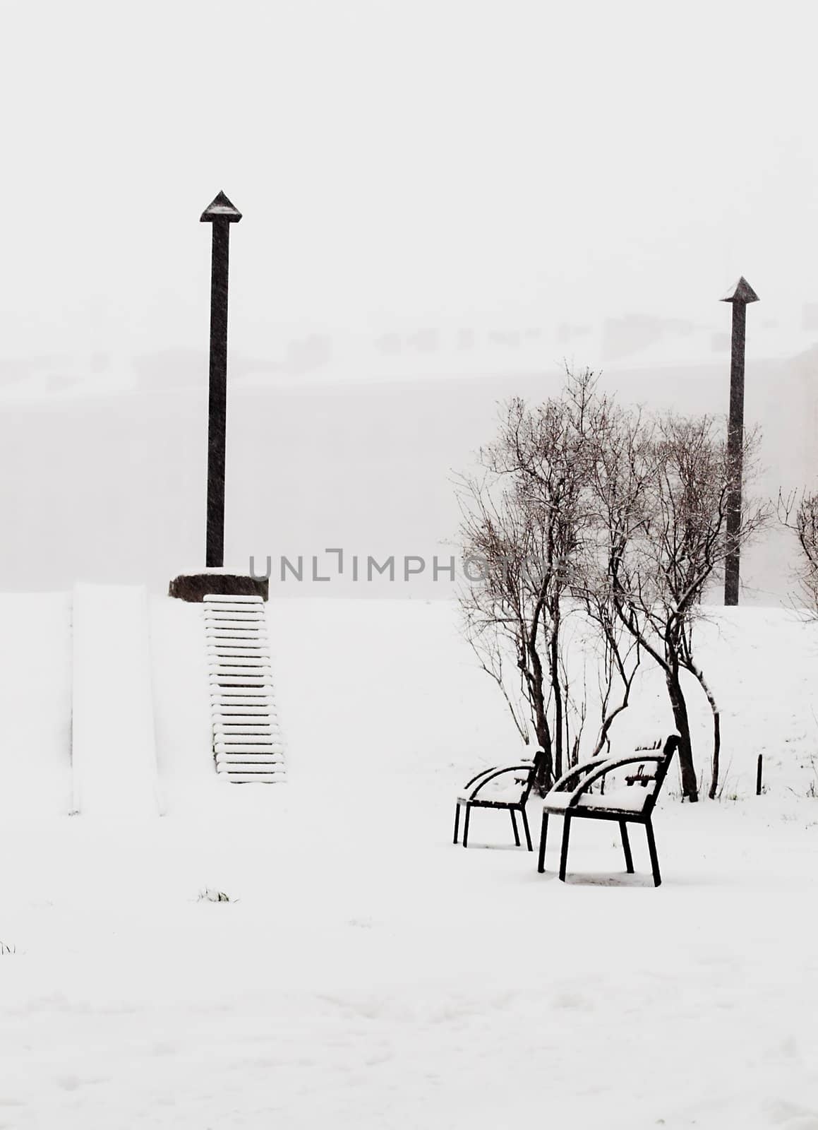 Benches at a back alley while snowing heavily.