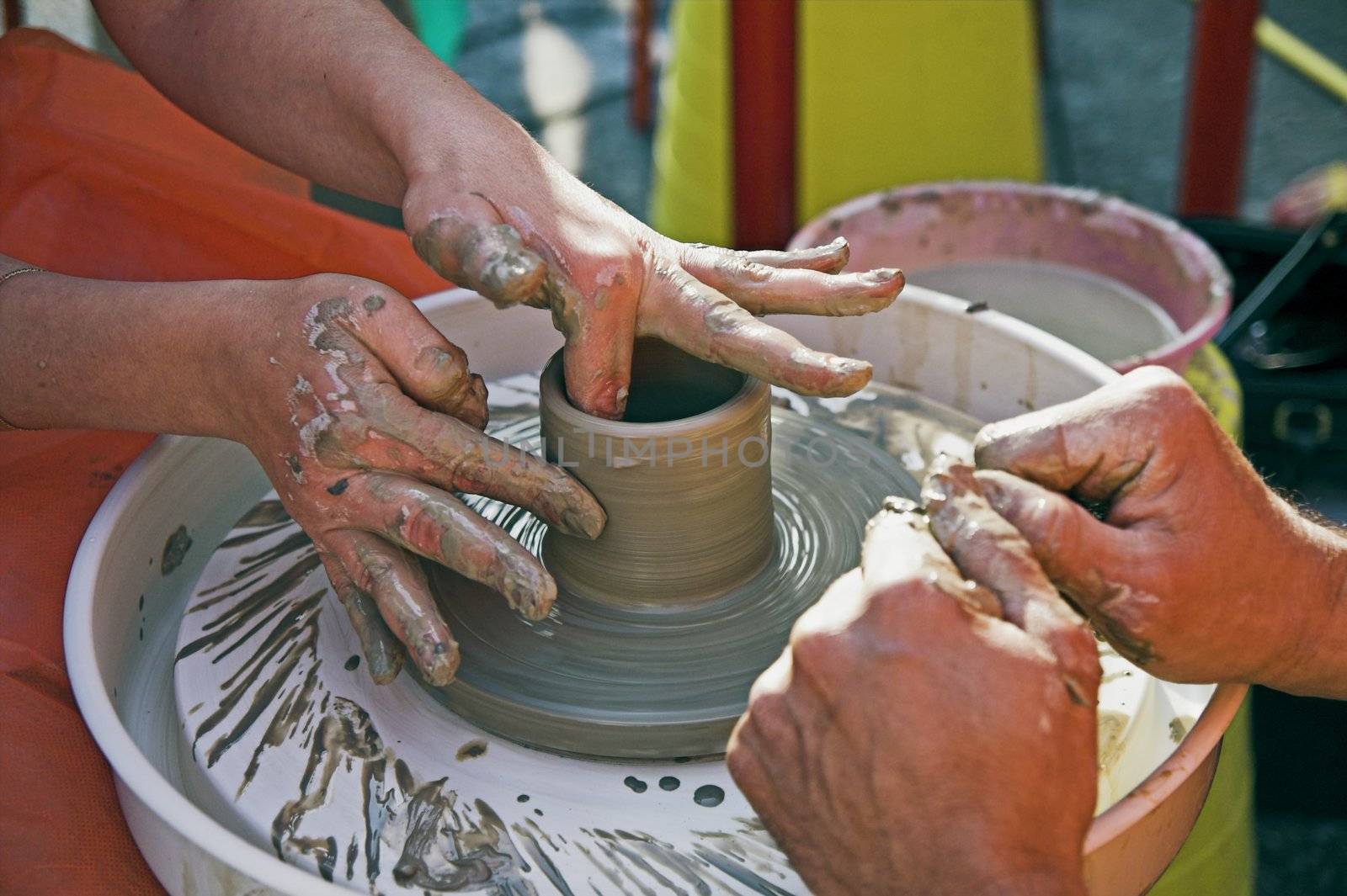 potter's hands guiding woman's hands to help her learn pottery