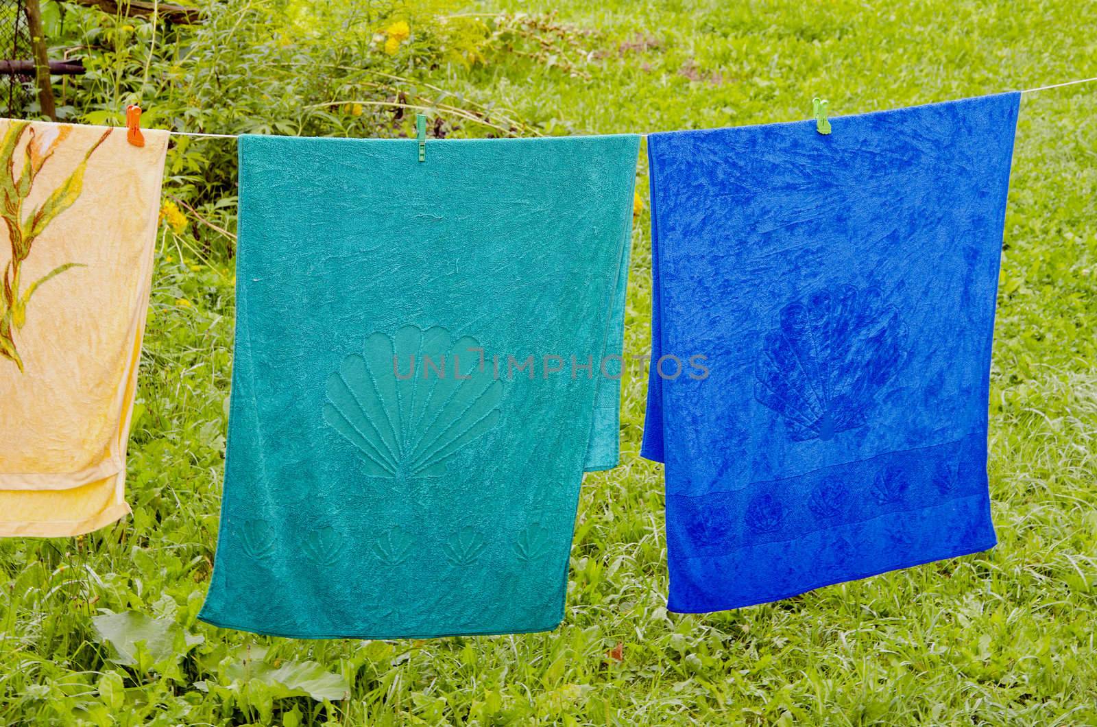 Multicolor towels atached with pins hanging on string in farmstead. Wooden fence in background.