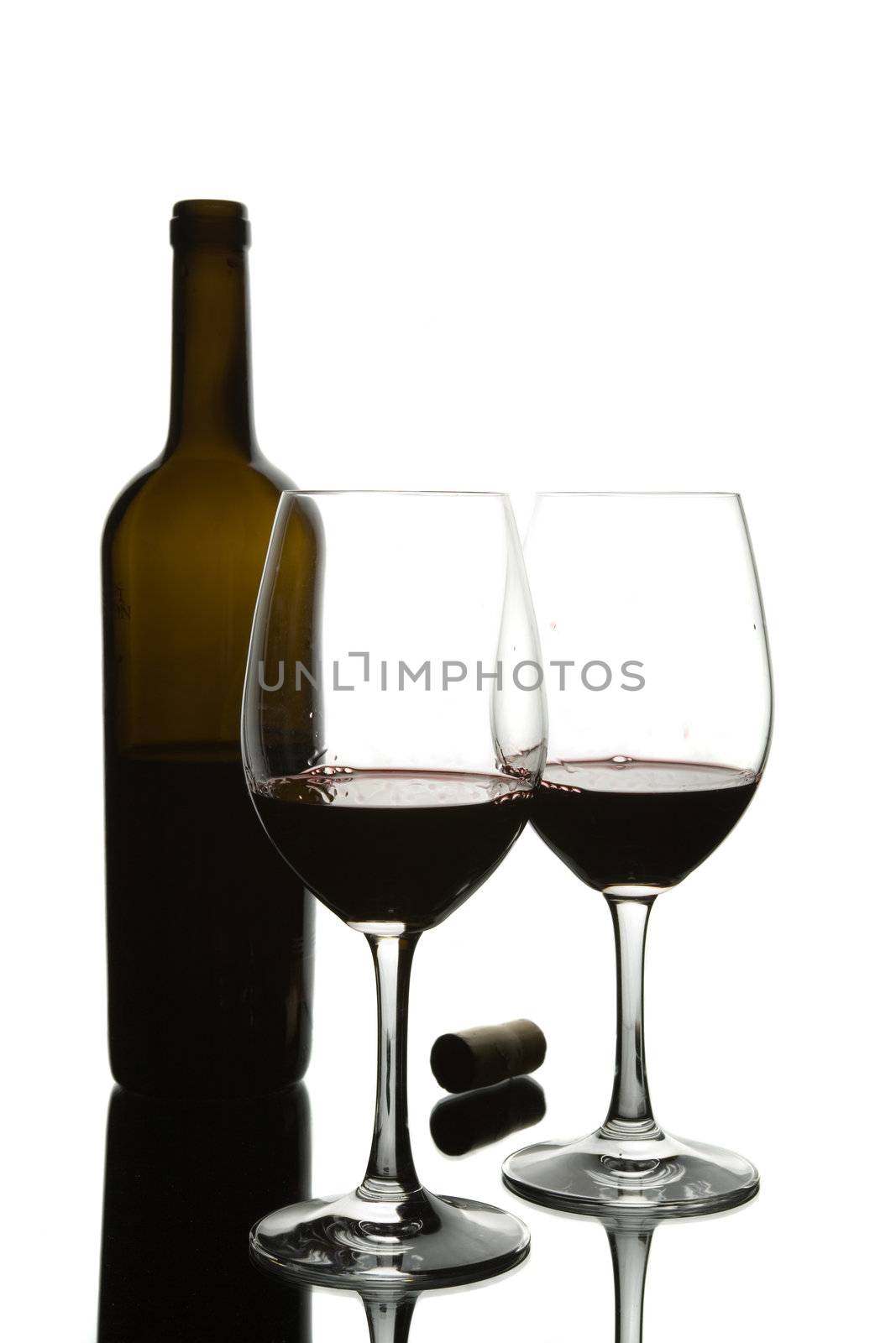 Two glasses of red wine and a translucent bottle