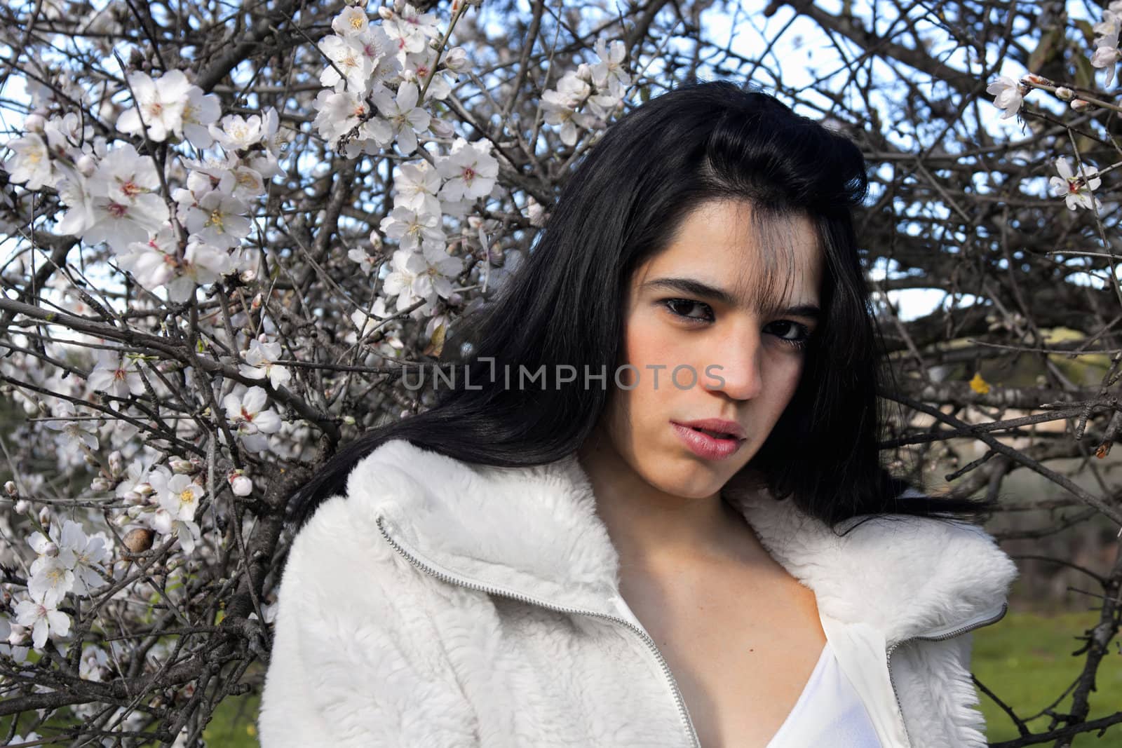 View of a beautiful girl on a white dress on a green grass field next to a almond tree