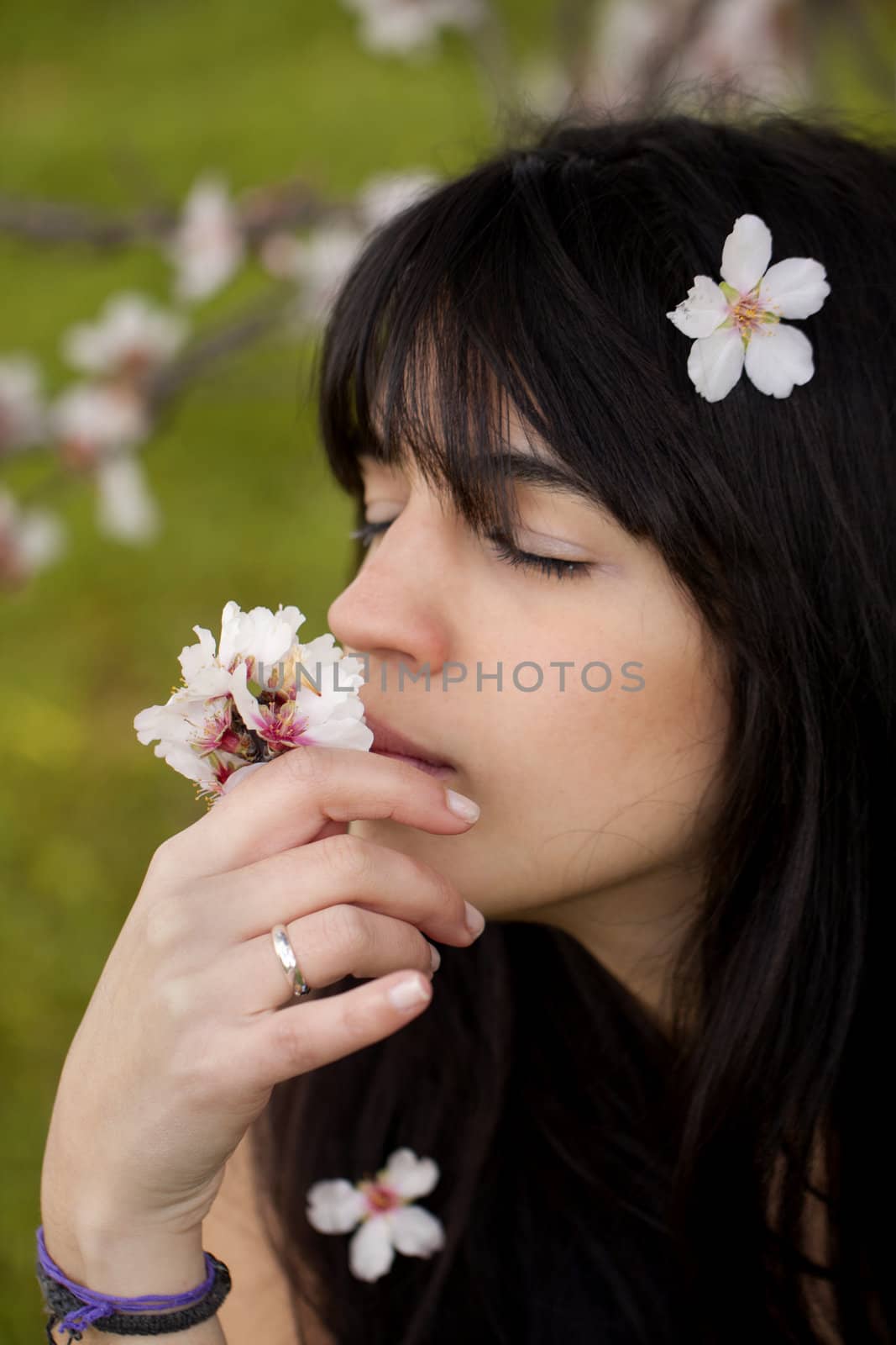 View of a beautiful girl on a white dress on a green grass field next to a almond tree