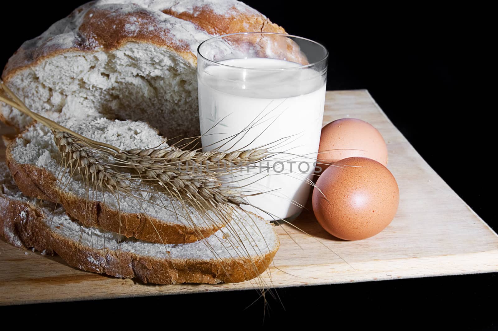Glass of milk, wheat, eggs and bread over wooden plate
