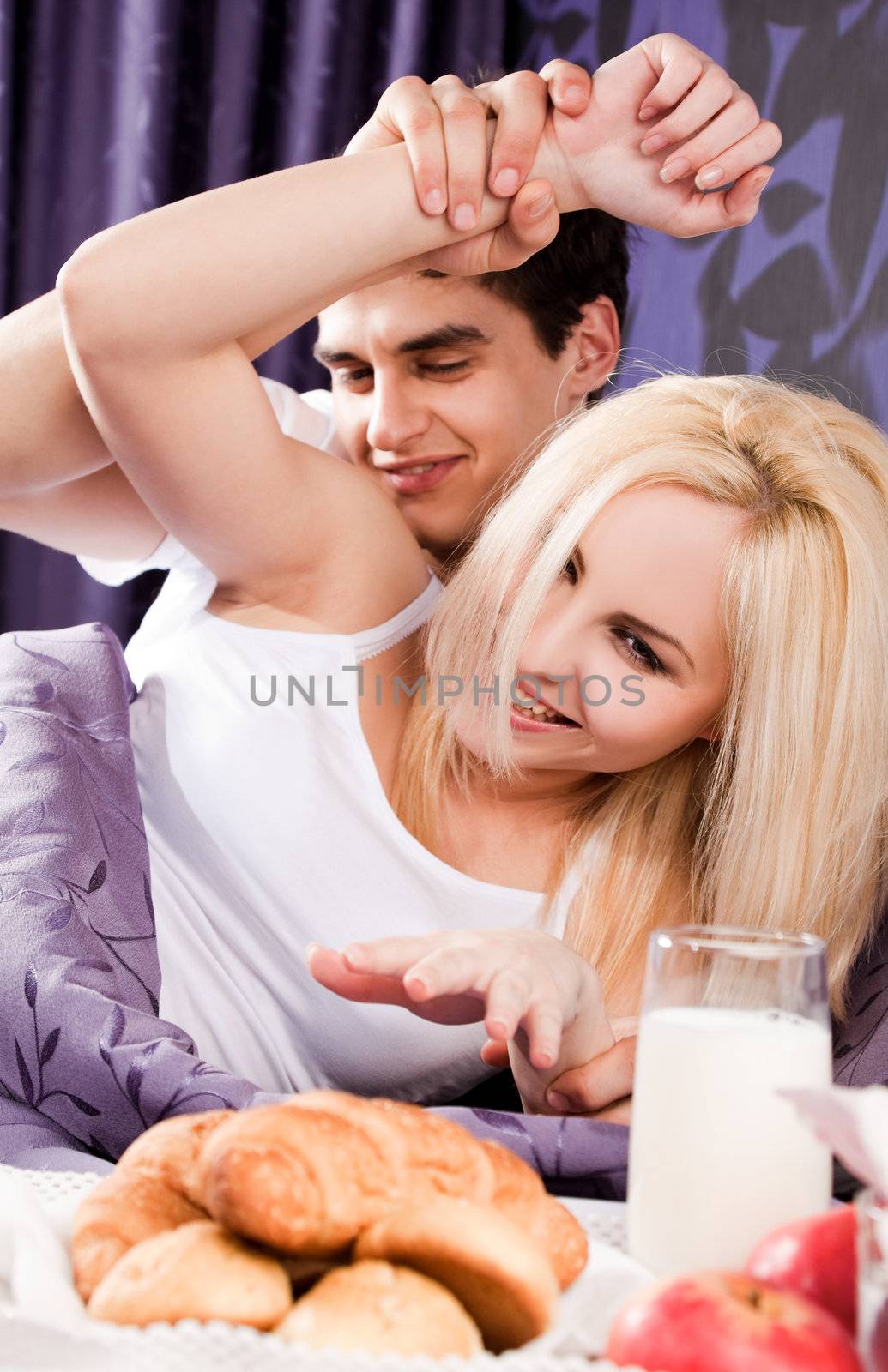 Young happy couple lying and having breakfast in bed
