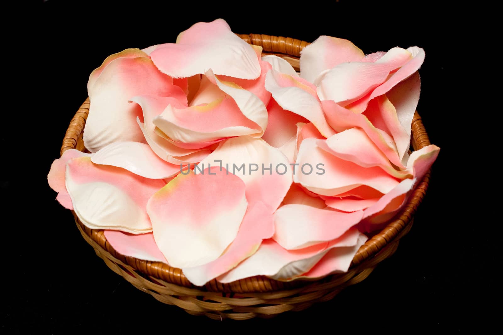 Artificial pink rose textile petals in basket on black
