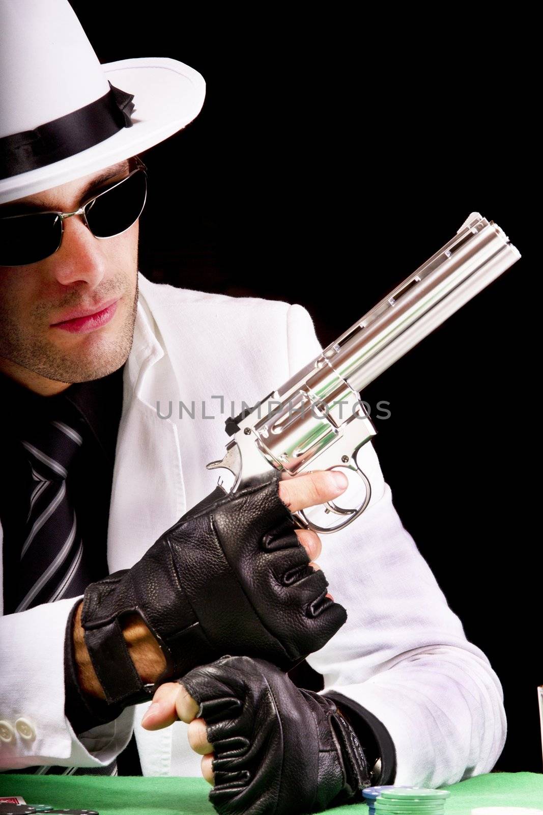 View of a gangster man playing some cards and poker,  holding a gun.