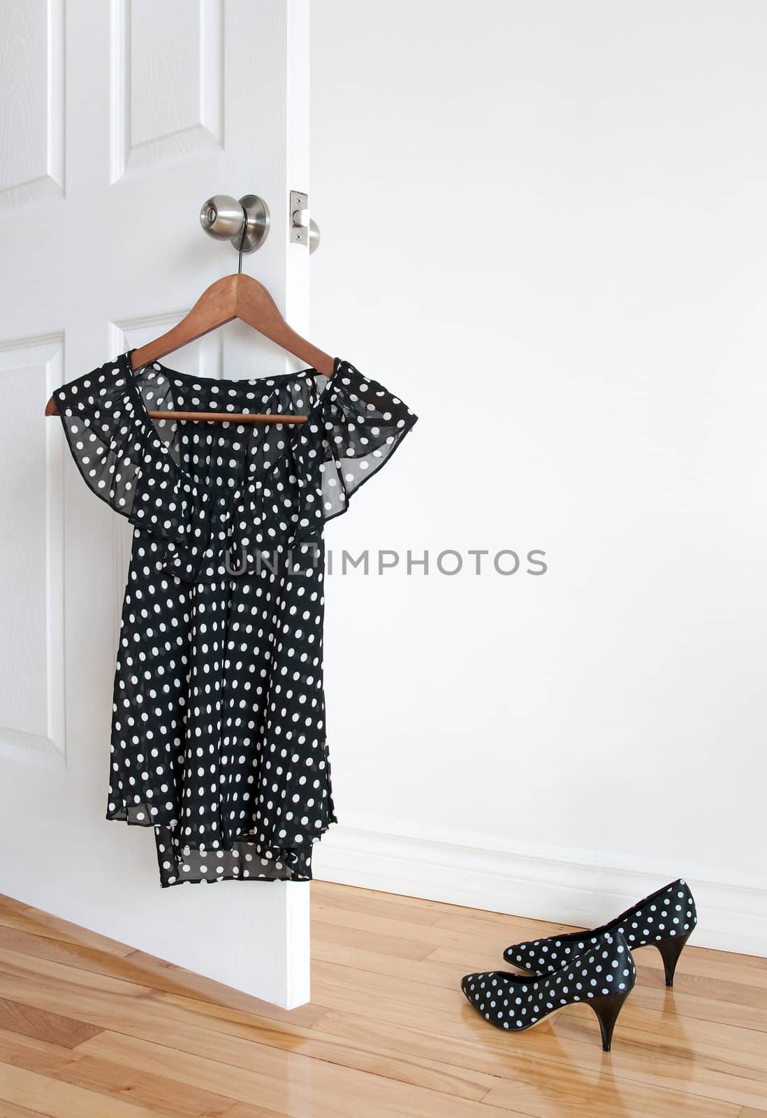 Black and white polka dot blouse on a hanger and shoes on wooden floor.