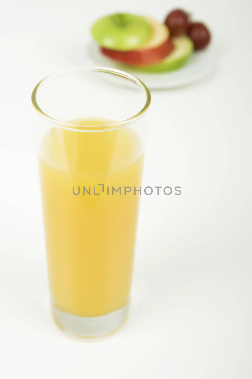 a glass of orange juice. A plate of fruit in the background
