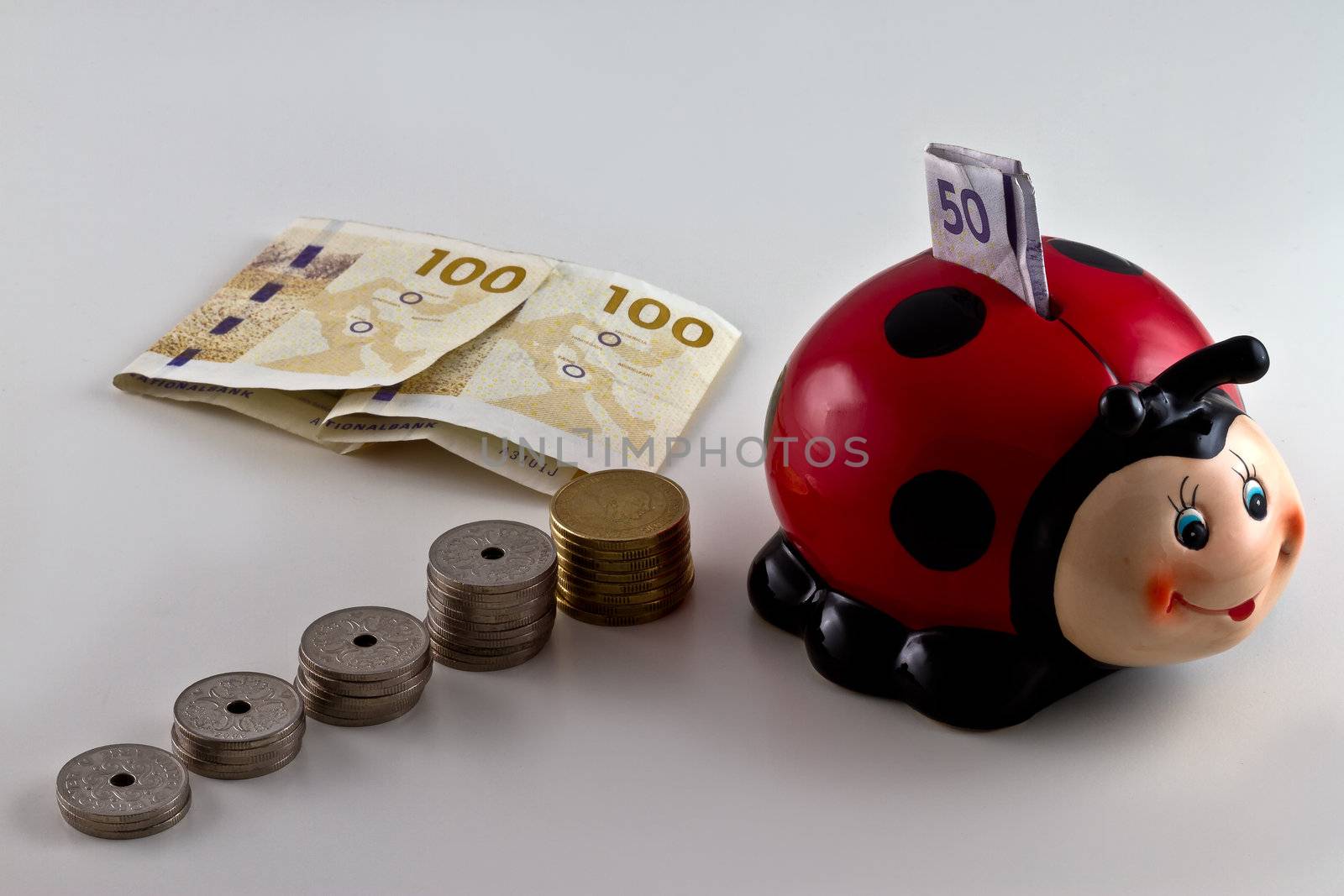 A piggy bank shaped as a ladybird with Danish currency around. isolated on light background
