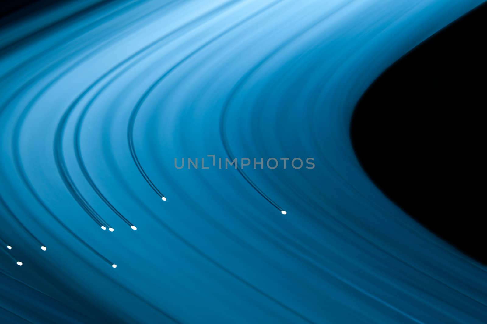 Close up capturing the ends of several illuminated fibre optic light strands against a vibrant blue background. Abstract style.