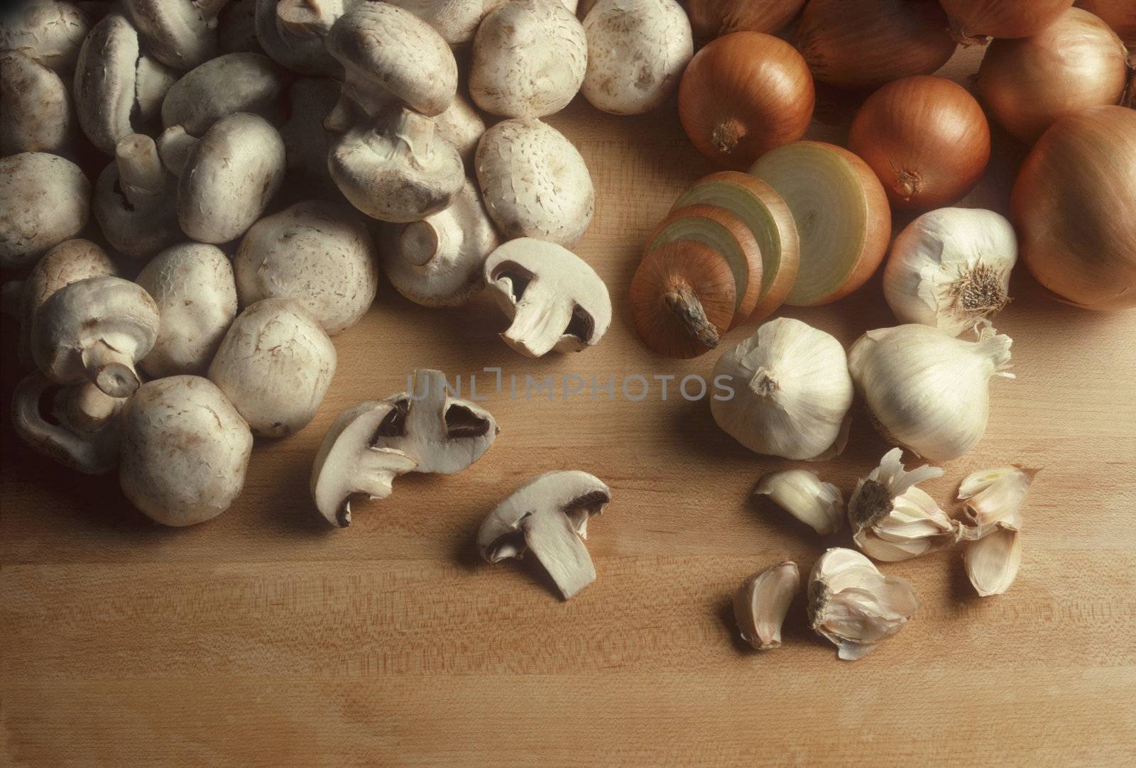 Mushrooms, onions and garlic on a wooden butcherblock surface