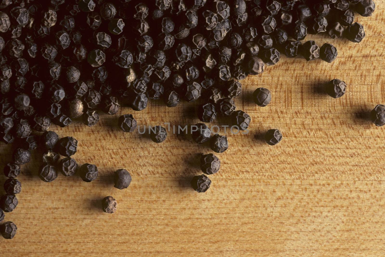 Whole black peppercorns on a wooden butcherblock surface